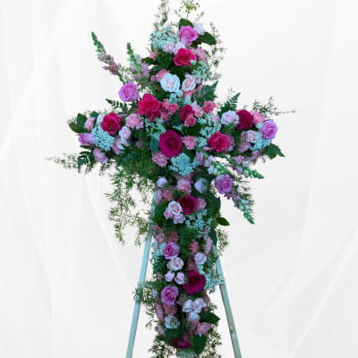 Tall floral cross covered in pink and white roses with greenery