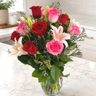 Bouquet of red and pink roses with white lilies in a clear glass vase