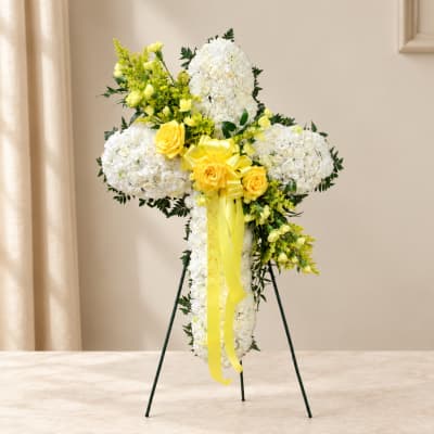 White floral standing cross with yellow roses and ribbon on an easel