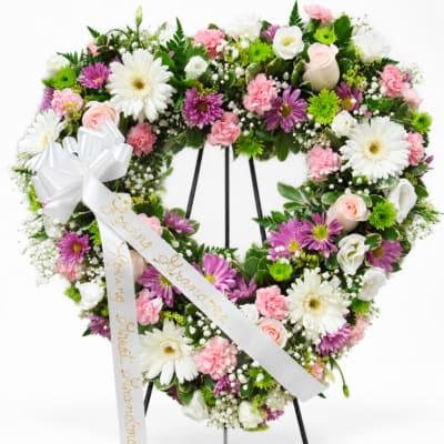 Heart-shaped floral wreath with pink, white, and purple flowers on a stand