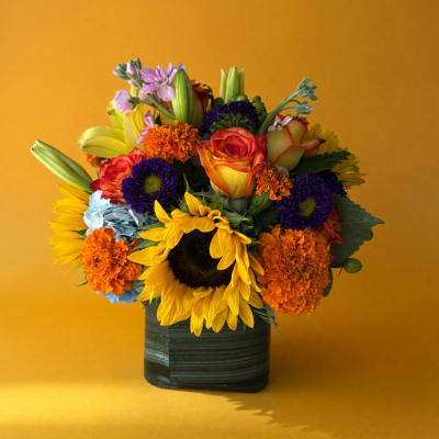 Colorful bouquet with sunflowers, roses, and mums in a dark square vase