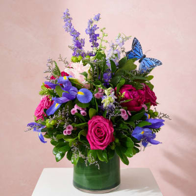 Colorful bouquet of roses, irises, and purple flowers in a glass vase with a blue butterfly