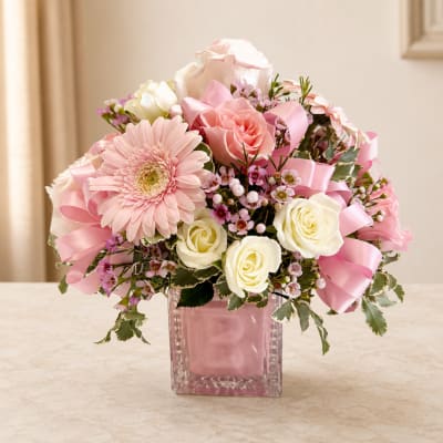 Pink and white flower arrangement in a square glass vase with ribbon