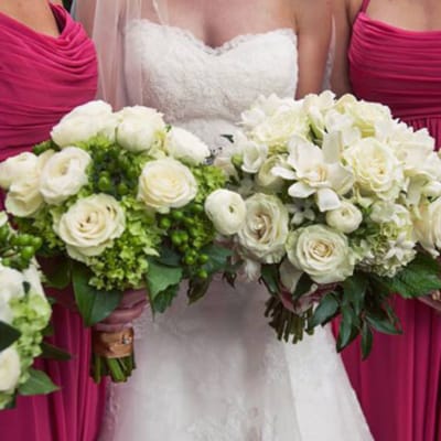 Bride holding white rose bouquets with bridesmaids in pink dresses