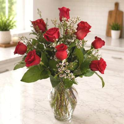 Red roses arranged in a clear glass vase with small white filler flowers