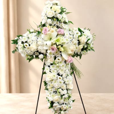 White floral cross arrangement on a stand with pale pink roses