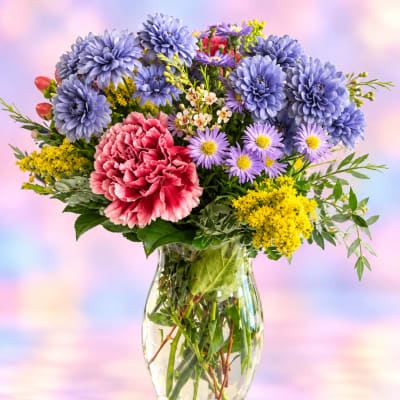 Mixed bouquet of blue, pink, and yellow flowers in a clear glass vase