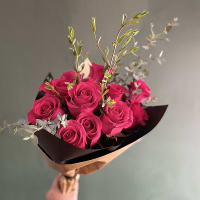 Bouquet of bright pink roses with airy greenery in dark wrap