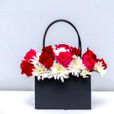 Black gift bag filled with red and pink roses and white daisies
