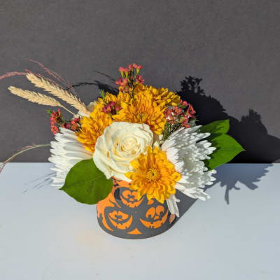 Yellow and white floral arrangement in a Halloween pumpkin container