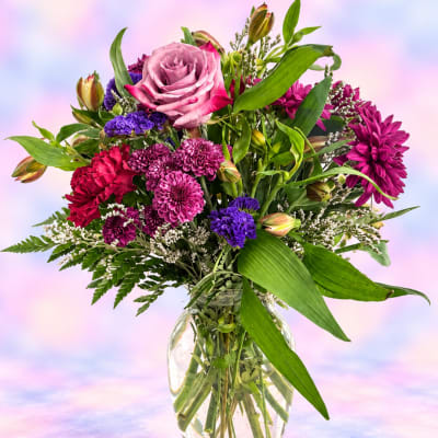 Mixed bouquet of pink, purple, and red flowers in a clear glass vase