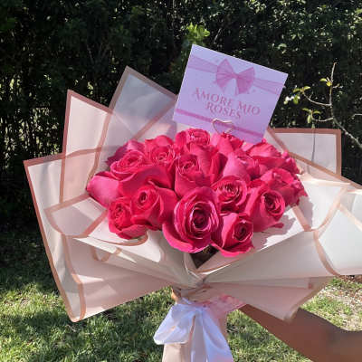 Bouquet of bright pink roses wrapped in blush paper with a white ribbon