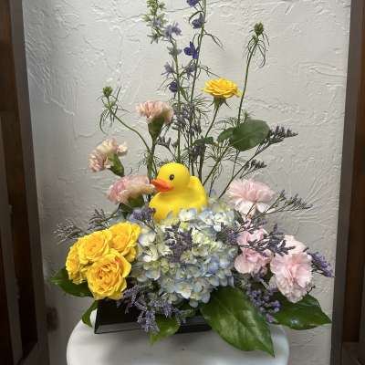 Floral arrangement with a yellow duck figurine in a black container