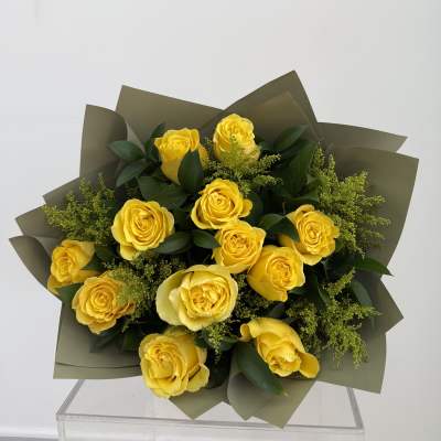 Bouquet of yellow roses with dark green foliage and olive wrapping