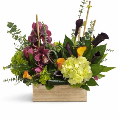 Arrangement of purple orchids, calla lilies, and green hydrangea in a wooden box
