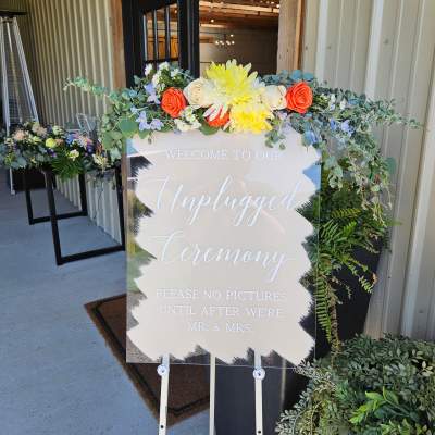 Floral sign topper with orange and yellow blooms and trailing greenery
