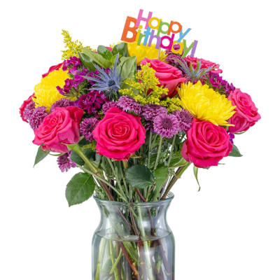 Bright mixed bouquet of pink roses and yellow chrysanthemums in a glass vase with a birthday sign