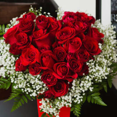 Red roses arranged in a tall red vase with white filler flowers