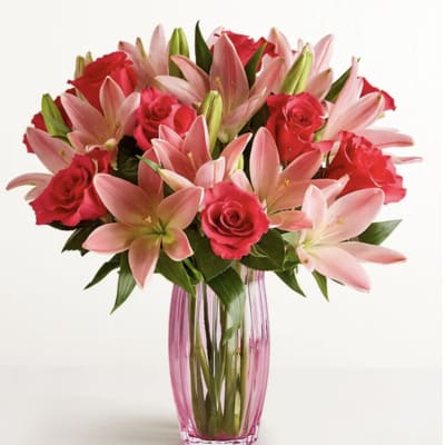 Pink lilies and red roses arranged in a pink glass vase