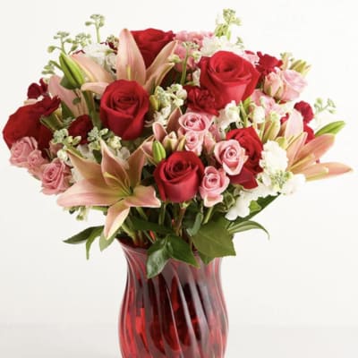 Red and pink roses with lilies in a red glass vase