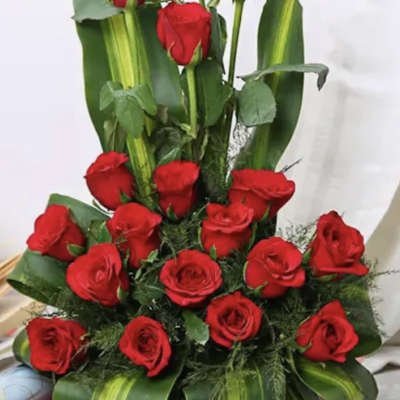 Red roses arranged in a basket with broad green leaves