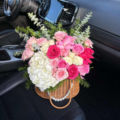 Pink and white rose bouquet in a wicker basket with greenery