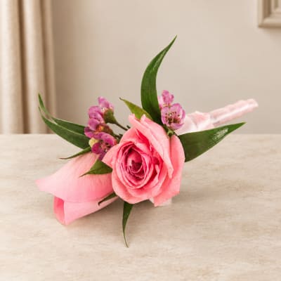Pink rose boutonniere with small purple flowers and green leaves