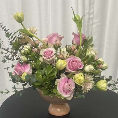 Pink roses and pale blooms arranged in a pedestal bowl vase