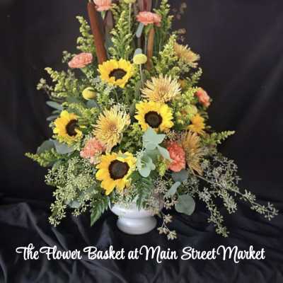 Tall floral arrangement with sunflowers, carnations, and a white vase
