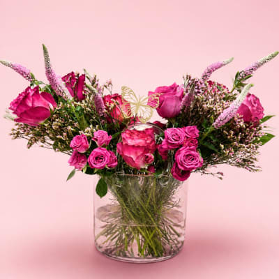 Pink roses and spray roses in a clear glass vase with a butterfly pick