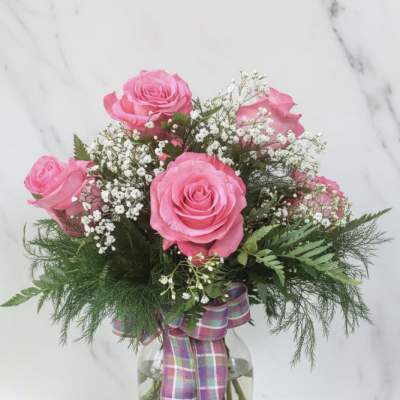 Pink roses in a glass vase with baby's breath and a plaid ribbon