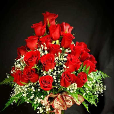 Red roses arranged in a glass vase with baby's breath and a ribbon