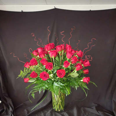 Red roses arranged in a clear glass vase with curly wire accents