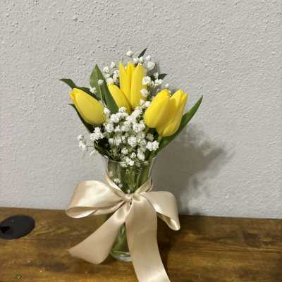 Yellow tulips in a glass vase with white baby's breath and a satin bow