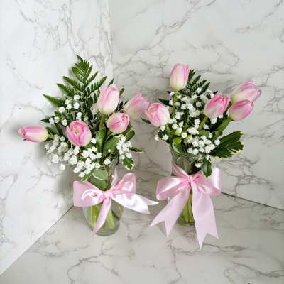 Two pink tulip bouquets in glass vases with pink ribbons