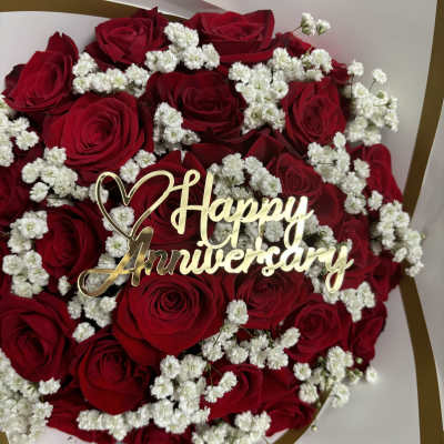 Red roses with white baby's breath and a gold Happy Anniversary topper