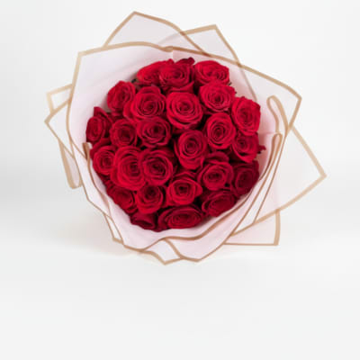 Round bouquet of red roses wrapped in white tissue and tan-edged paper