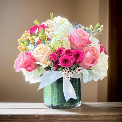 Pink and white rose bouquet in a glass vase with a white ribbon