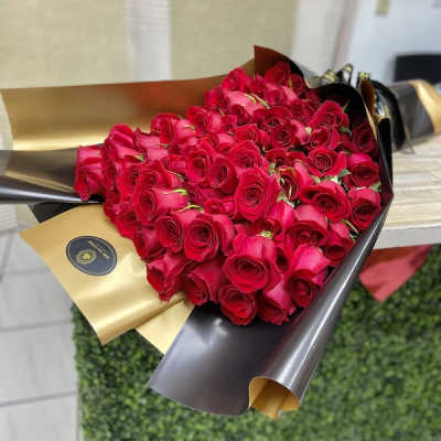 Large bouquet of tightly clustered red roses wrapped in glossy black and gold paper