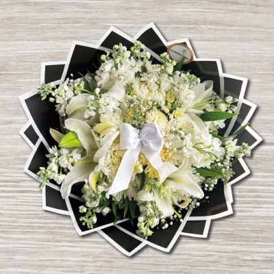 White floral bouquet with lilies and a satin bow on black wrap