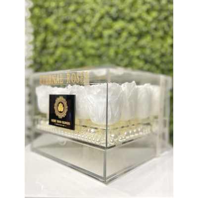 Clear acrylic box filled with white preserved roses arranged above a layer of pearls.