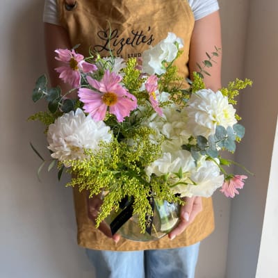Pink and white flowers arranged in a glass vase with greenery