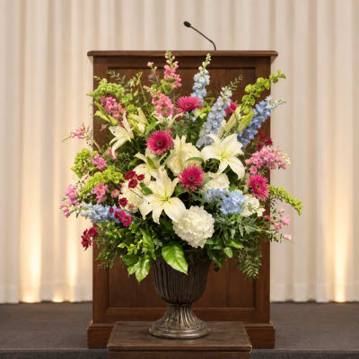 Large mixed floral arrangement in a dark urn on a podium