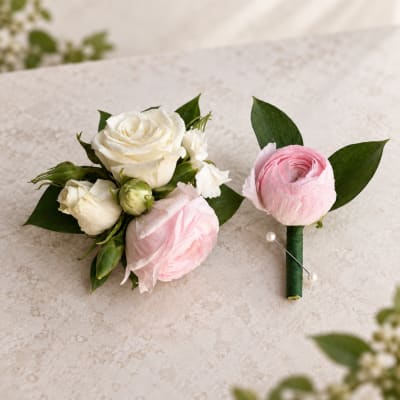 Two floral boutonnieres with pink and white blooms on a light stone surface