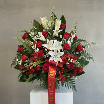 Red roses and white lilies arranged in a vase with a red ribbon