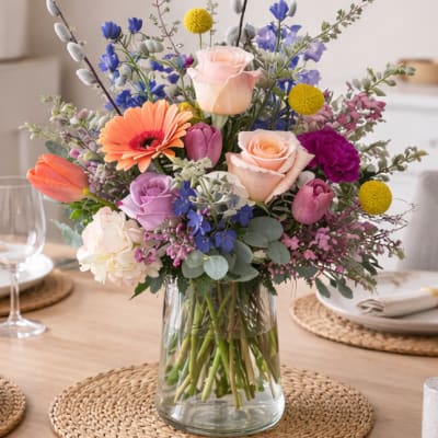 Mixed bouquet of roses, tulips, and daisies in a clear glass vase