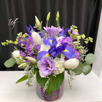 Purple and white floral arrangement in a mosaic glass vase