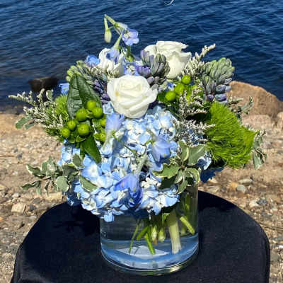 Blue and white floral arrangement in a glass vase by the water