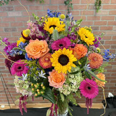 Colorful mixed bouquet with sunflowers, roses, and gerbera daisies in a glass vase