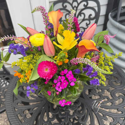 Colorful mixed bouquet in a glass vase with tulips, calla lilies, and daisies